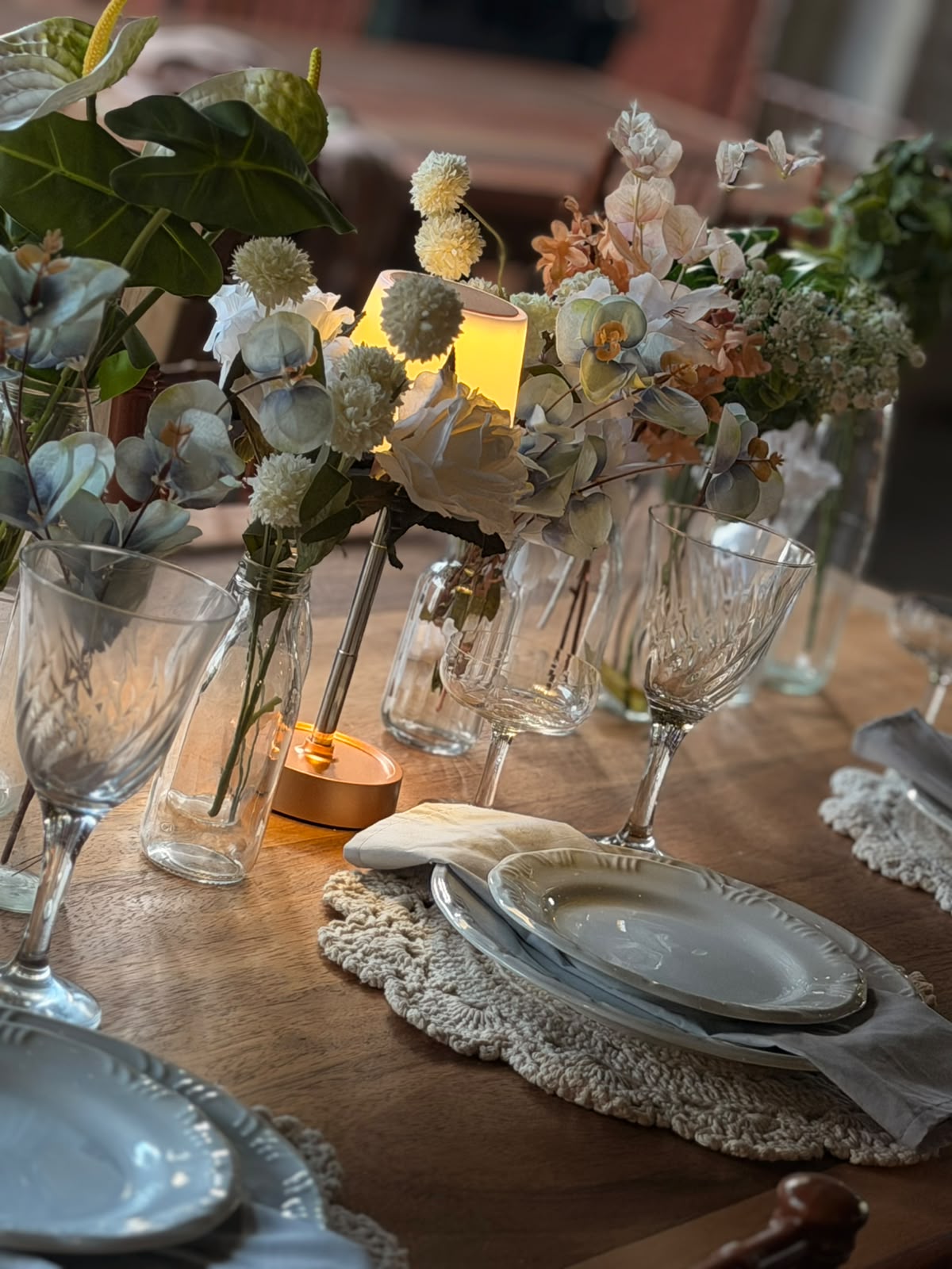 Centro de mesa com flores delicadas, luminária dourada e taças de cristal